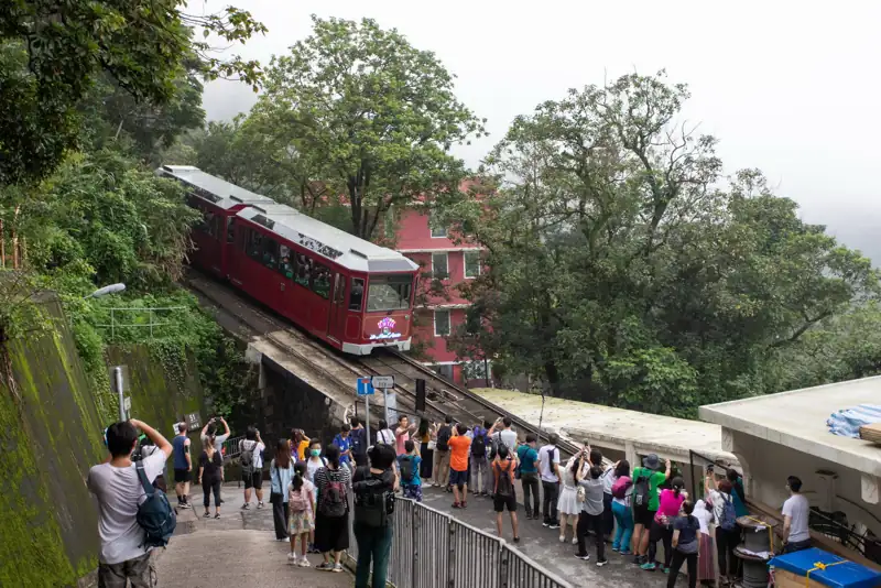 紅色山頂纜車駛過山坡，一班遊客喺路邊影相